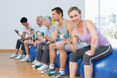 Class with dumbbells sitting on exercise balls in gym