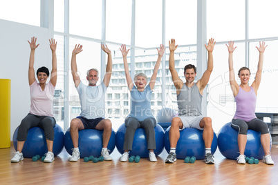 Class sitting on exercise balls and raising hands in gym
