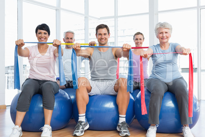 Class holding exercise belts while sitting on fitness balls