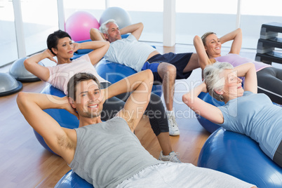 Smiling people stretching on exercise balls in gym