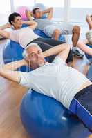 Smiling people stretching on exercise balls in gym