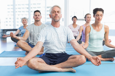 People in lotus pose with eyes closed at fitness studio