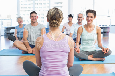 Sporty people sitting on exercise mats at fitness studio