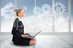 Blonde businesswoman sitting using laptop with cogs and wheels