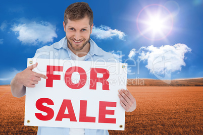 Composite image of smiling model holding a for sale sign