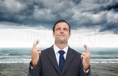 Composite image of serious businessman with fingers crossed is l