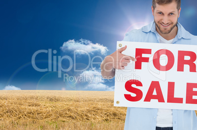 Composite image of smiling model holding a for sale sign