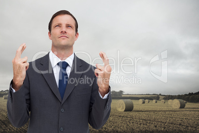 Composite image of serious businessman with fingers crossed is l