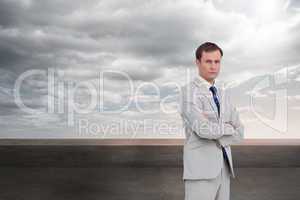 Composite image of serious businessman standing with his arms fo