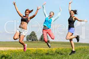 sporty friends jumping cheerful on sunny meadow