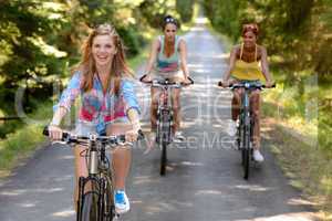 three female friends riding bikes in park