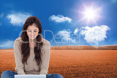 Composite image of brunette sitting on floor using laptop