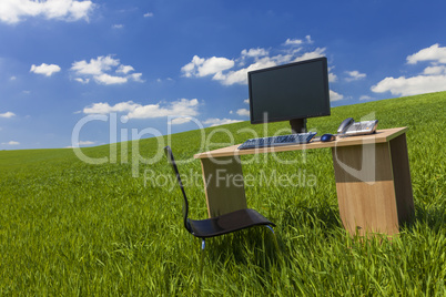 desk and computer in green field with blue sky