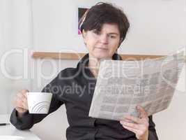 woman relaxing drinking a cup of coffee and reading newspaper