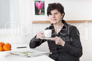 woman relaxing drinking a cup of coffee and reading newspaper