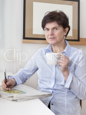 woman relaxing drinking a cup of coffee and reading newspaper