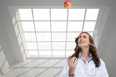 Composite image of happy doctor throwing apple