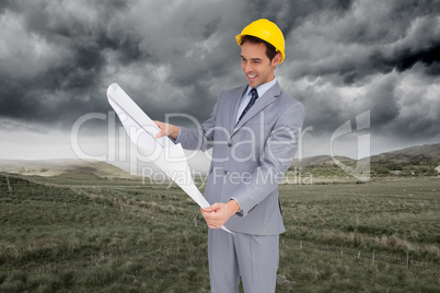 Composite image of smiling architect with hard hat looking at pl