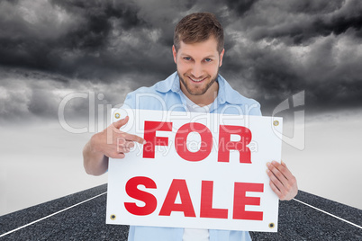 Composite image of smiling model holding a for sale sign
