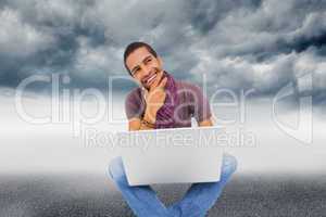 Composite image of thinking man sitting on floor using laptop an
