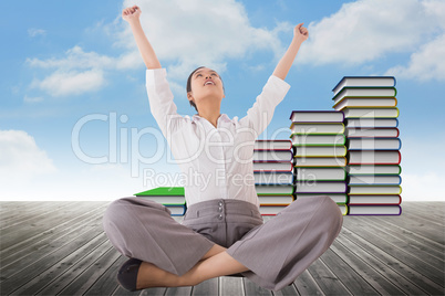 Composite image of cheering businesswoman sitting cross legged