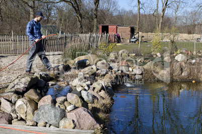 man with hose on the garden pond