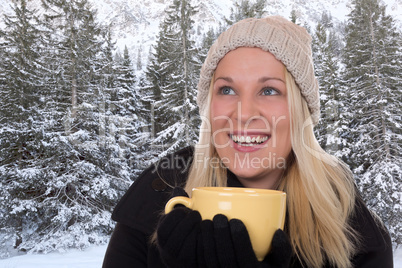 Junge blonde Frau trinkt draußen im Winter eine Tasse Tee