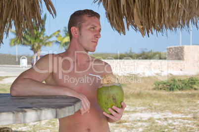 Junger Mann trinkt im Urlaub aus Kokosnuss