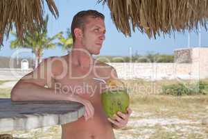 Junger Mann trinkt im Urlaub aus Kokosnuss