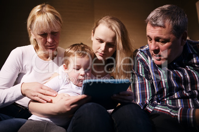 family watching boy playing game on touchpad