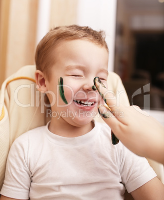 little boy laughing as his mother paints his face