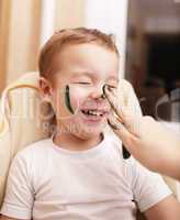 little boy laughing as his mother paints his face