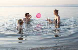 young family playing with ball at sunset