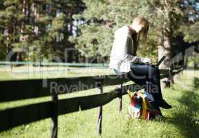 young woman sitting on a rustic fence