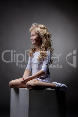 Joyful blonde gymnast posing on cube in studio