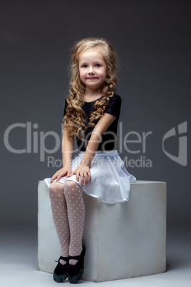 Smiling cute girl posing sitting on cube in studio