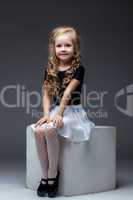 Smiling cute girl posing sitting on cube in studio