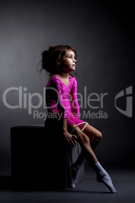 Sad artistic gymnast sitting on cube with rope