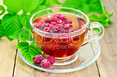 Tea with raspberry and green leaves on board