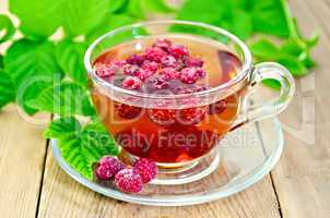Tea with raspberry and green leaves on board