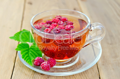 Tea with raspberry and leaf in a cup on board