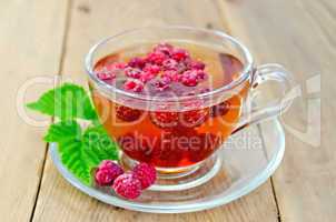 Tea with raspberry and leaf in a cup on board