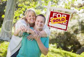 Couple In Front of Sold Real Estate Sign Holding Keys