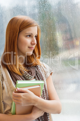 thoughtful student with books by window