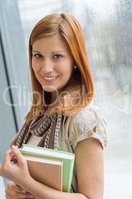 smiling student holding books by window