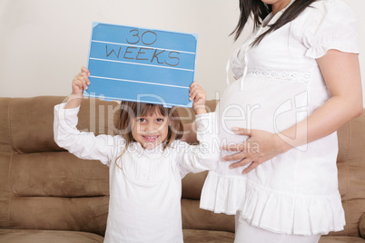 girl holding a 30 weeks sign to her expectant mother