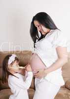 girl listens to a stethoscope belly of her pregnant mom