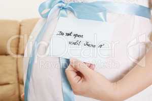 pregnant belly with a light blue ribbon and a tag saying do not