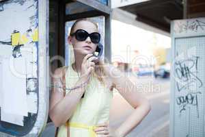 young woman standing chatting on a public phone