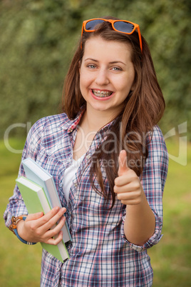 student with braces showing thumb up outside